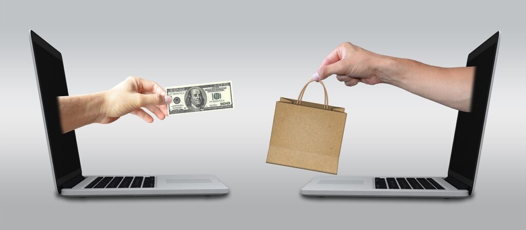Hand holding money reaching out of laptop toward hand holding shopping bag coming out of another laptop